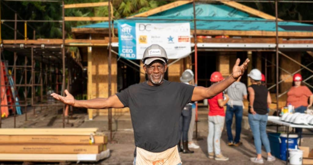 Homeowner Randy Brown stands arms outstretched in front of a home under construction